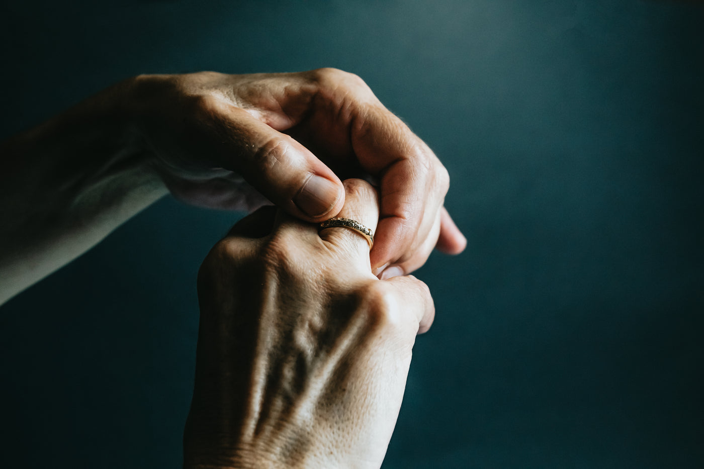 A hand turning a plain band on the finger against a dark ground