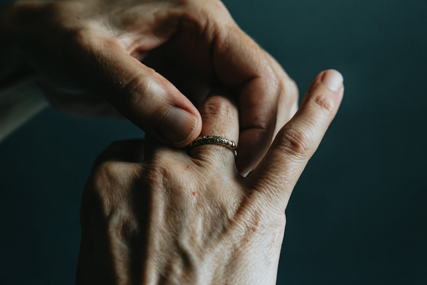 A hand wearing two textured bands against a dark green ground