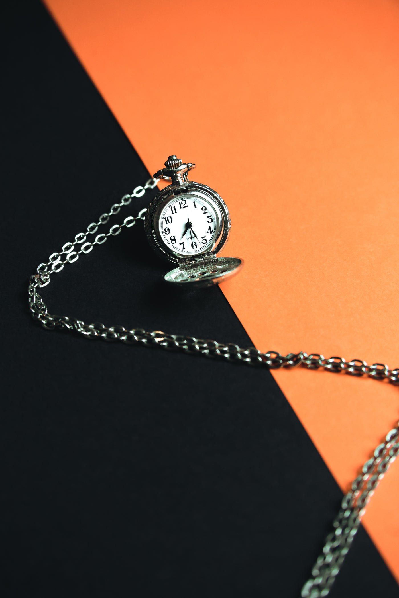 Silver pocket watch open on its chain against an orange and black ground